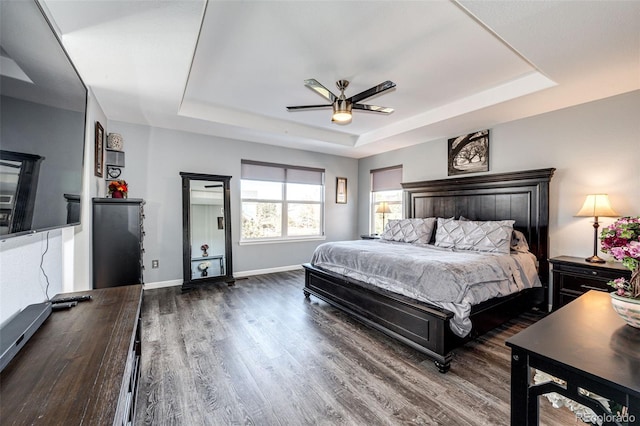 bedroom with dark hardwood / wood-style floors, ceiling fan, and a tray ceiling