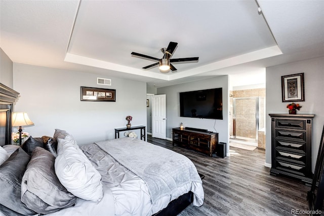 bedroom featuring ceiling fan, ensuite bathroom, dark hardwood / wood-style floors, and a raised ceiling