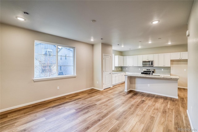 23981 E 40th Ave, Aurora, CO 80019 - kitchen featuring stainless steel microwave, stove, light wood finished floors, white cabinetry, and backsplash