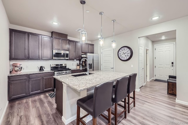 6153 N Ceylon St Unit 2-202, Denver, CO 80249 - kitchen featuring stainless steel appliances, dark brown cabinets, light wood finished floors, a breakfast bar, and an island with sink