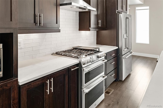 1615 Harlan St Unit 2, Lakewood, CO 80214 - kitchen featuring high end appliances, wall chimney range hood, dark brown cabinets, backsplash, and dark wood-type flooring