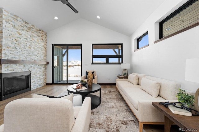 living room featuring a stone fireplace, a healthy amount of sunlight, high vaulted ceiling, and wood finished floors