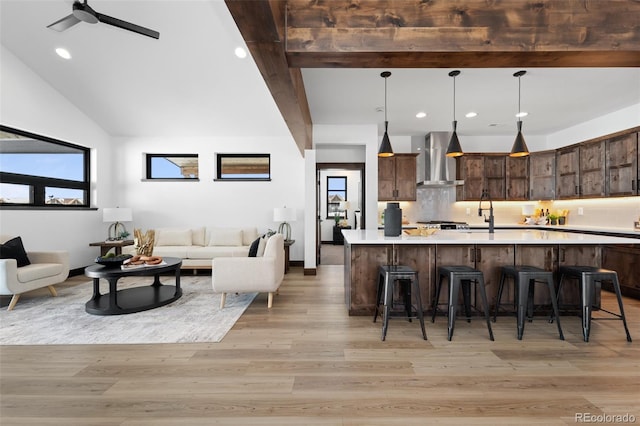 kitchen featuring light wood finished floors, backsplash, a breakfast bar area, light countertops, and wall chimney exhaust hood