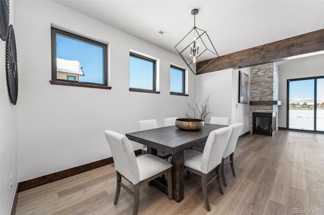 dining room with visible vents, a glass covered fireplace, light wood finished floors, baseboards, and a chandelier