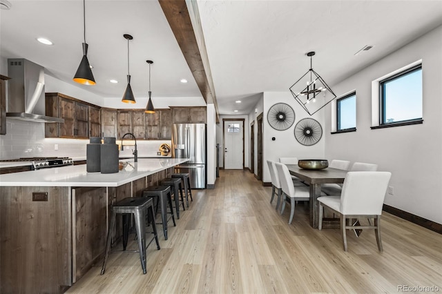 kitchen with decorative backsplash, stainless steel fridge, wall chimney exhaust hood, and light wood-style flooring