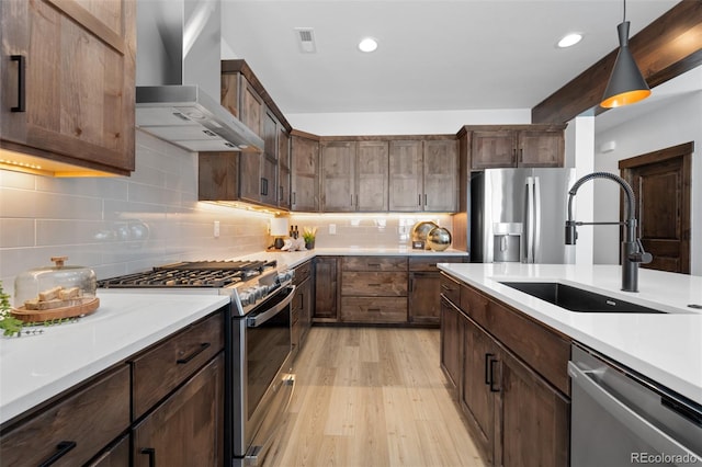 kitchen with light countertops, light wood-style flooring, appliances with stainless steel finishes, wall chimney exhaust hood, and a sink