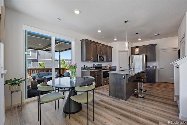 1100 Blue Bell Rd, Berthoud, CO 80513 - kitchen with appliances with stainless steel finishes, dark brown cabinetry, a breakfast bar area, light wood finished floors, and a sink
