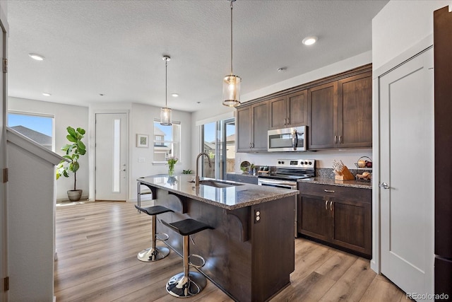 1100 Blue Bell Rd, Berthoud, CO 80513 - kitchen with stainless steel appliances, a sink, light wood finished floors, dark stone countertops, and a kitchen breakfast bar