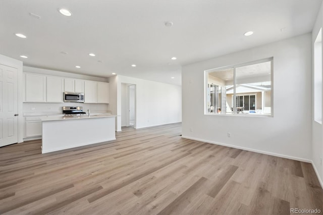 kitchen featuring stainless steel appliances, light wood-type flooring, a center island with sink, and white cabinets