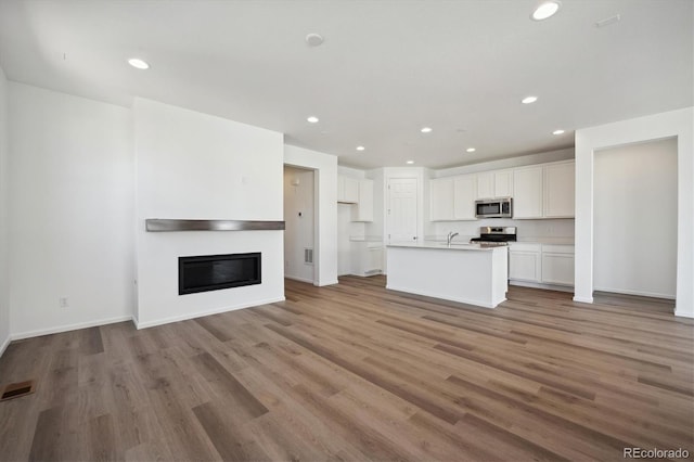 kitchen with a center island with sink, appliances with stainless steel finishes, white cabinets, and light hardwood / wood-style floors