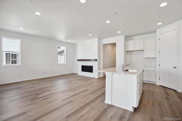 kitchen featuring white cabinetry, light hardwood / wood-style floors, sink, and a kitchen island with sink