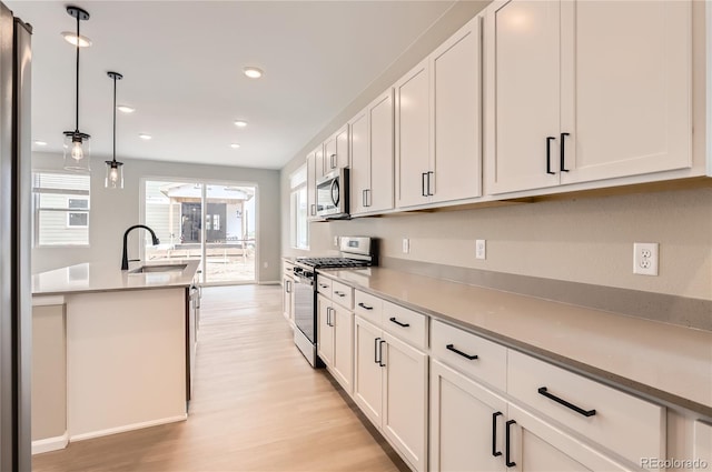 4102 Estrella St, Brighton, CO 80601 - kitchen with stainless steel appliances, light wood-style floors, white cabinets, decorative light fixtures, and recessed lighting