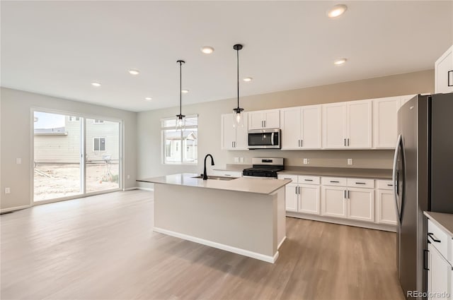 4102 Estrella St, Brighton, CO 80601 - kitchen featuring stainless steel appliances, light wood-style floors, white cabinetry, hanging light fixtures, and an island with sink