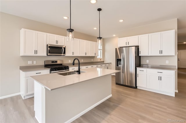 4102 Estrella St, Brighton, CO 80601 - kitchen featuring appliances with stainless steel finishes, light wood-style flooring, white cabinets, pendant lighting, and an island with sink