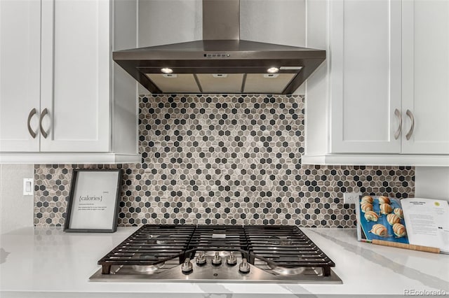 interior details with backsplash, wall chimney exhaust hood, white cabinetry, and stainless steel gas stovetop