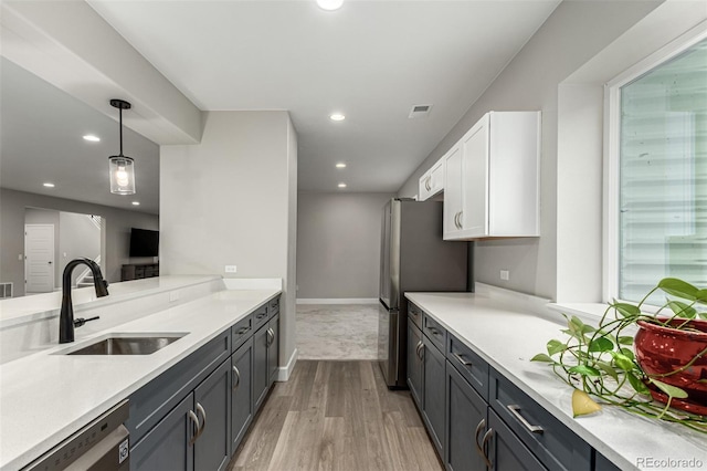 kitchen featuring a sink, stainless steel appliances, light wood finished floors, light countertops, and white cabinetry