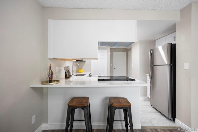 2856 S Kenton Ct, Aurora, CO 80014 - kitchen with freestanding refrigerator, white cabinets, light countertops, a kitchen bar, and a peninsula