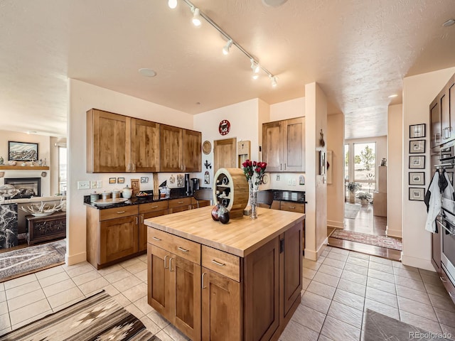 kitchen featuring a center island, a fireplace, brown cabinetry, light tile patterned flooring, and butcher block countertops