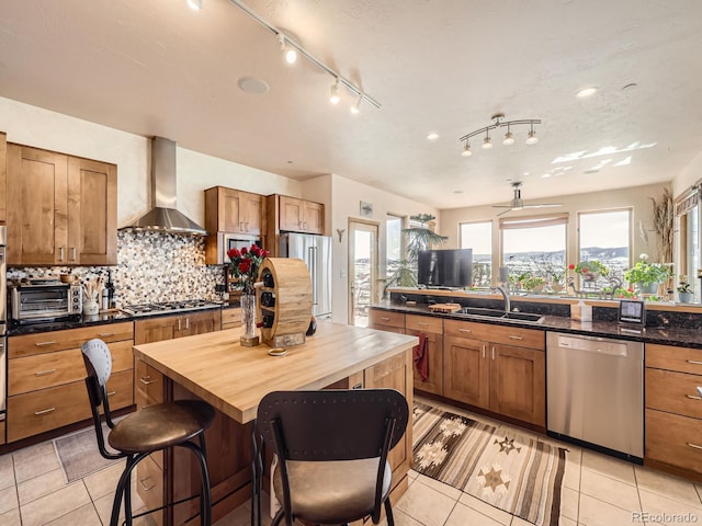 kitchen with light tile patterned floors, tasteful backsplash, appliances with stainless steel finishes, a sink, and wall chimney range hood