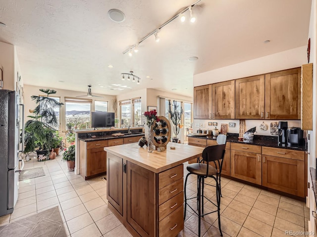 kitchen with light tile patterned flooring, wood counters, freestanding refrigerator, and a healthy amount of sunlight