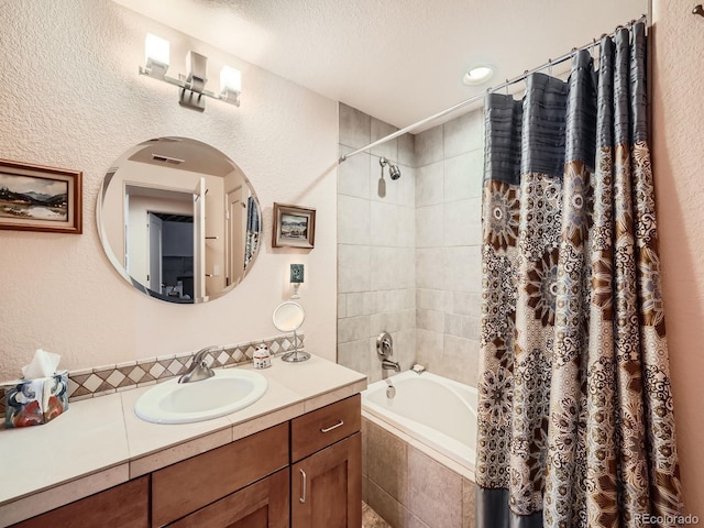 bathroom with a textured wall, tiled shower / bath combo, vanity, and a textured ceiling