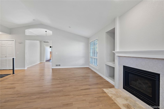 unfurnished living room featuring built in features, a chandelier, light hardwood / wood-style floors, vaulted ceiling, and a fireplace