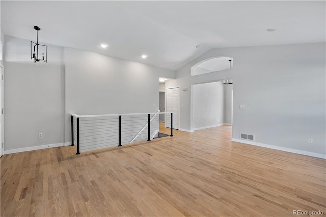 spare room featuring vaulted ceiling, a notable chandelier, and light wood-type flooring