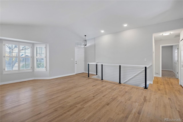 empty room featuring light hardwood / wood-style flooring, vaulted ceiling, and a chandelier