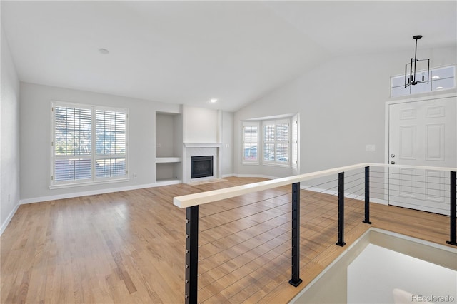 unfurnished living room with light wood-type flooring, an inviting chandelier, vaulted ceiling, and a healthy amount of sunlight