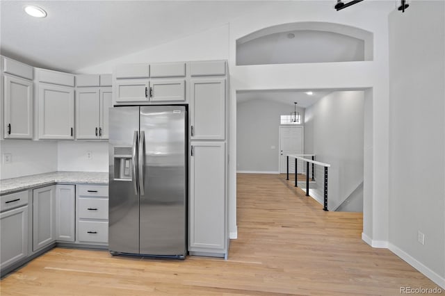 kitchen with a barn door, lofted ceiling, light wood-type flooring, and stainless steel fridge