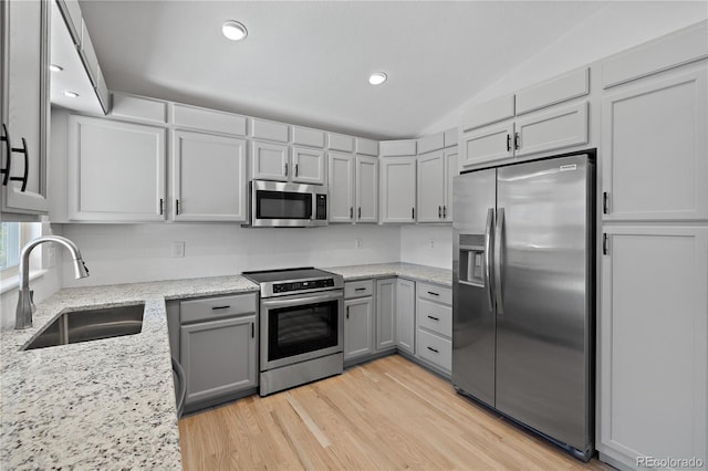 kitchen with sink, lofted ceiling, light wood-type flooring, light stone countertops, and stainless steel appliances