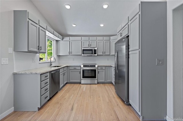 kitchen featuring light stone countertops, appliances with stainless steel finishes, light wood-type flooring, sink, and gray cabinets