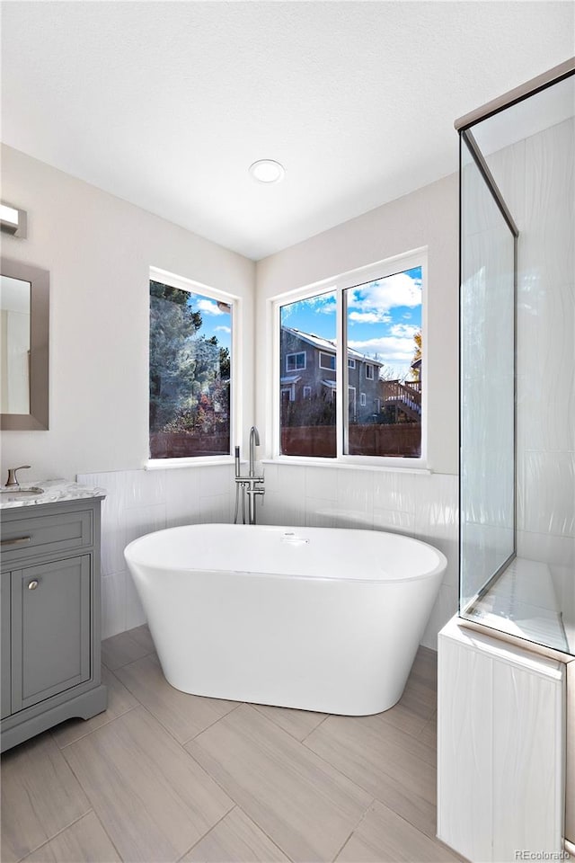 bathroom with a bathtub, vanity, tile walls, and tile patterned flooring