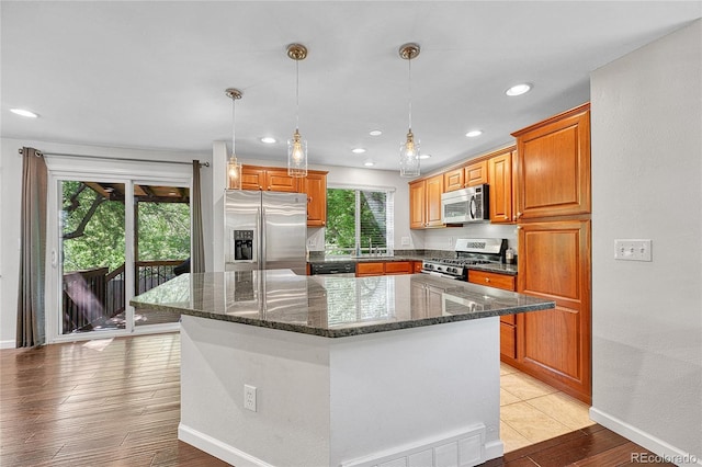 8032 Lee Ct, Arvada, CO 80005 - kitchen with appliances with stainless steel finishes, a center island, dark stone counters, light wood-type flooring, and pendant lighting
