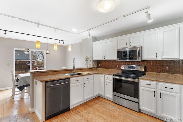 kitchen featuring white cabinets, stainless steel appliances, hanging light fixtures, and light hardwood / wood-style floors