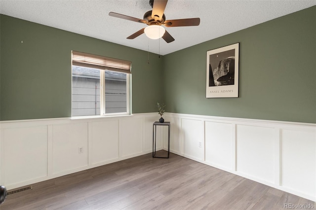 empty room with a textured ceiling, light wood-type flooring, and ceiling fan