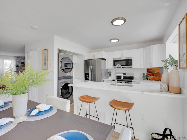 kitchen with appliances with stainless steel finishes, estacked washer and dryer, a peninsula, and white cabinets