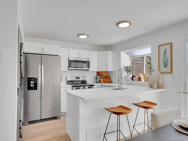 kitchen featuring stainless steel appliances, a sink, a breakfast bar area, and white cabinets