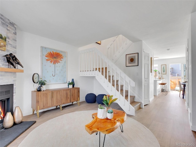 entrance foyer with light wood-style flooring, stairway, a large fireplace, and baseboards