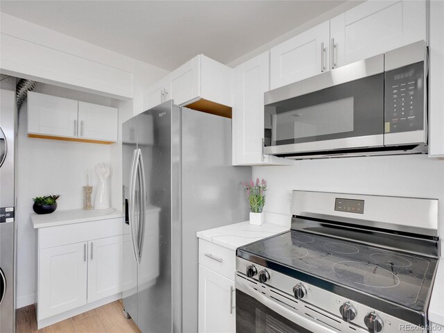 kitchen with appliances with stainless steel finishes, stacked washer / dryer, white cabinets, light wood-type flooring, and light stone counters