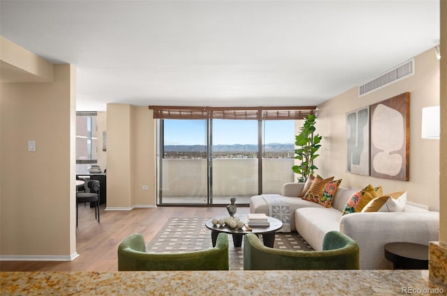 living room with a mountain view, baseboards, visible vents, a wall of windows, and wood finished floors