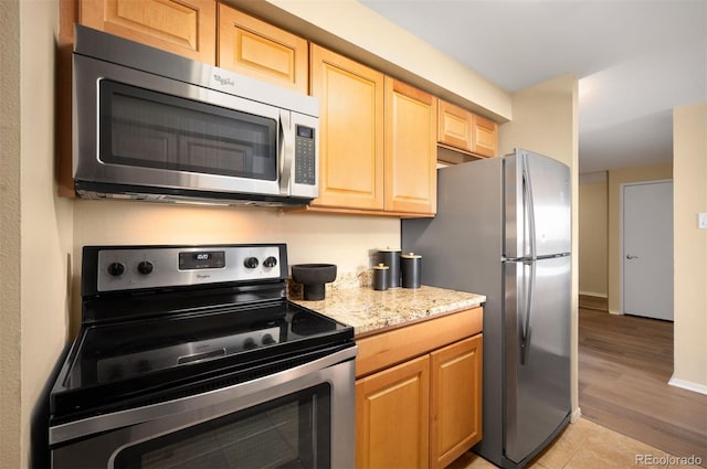 kitchen featuring stainless steel appliances, light brown cabinets, baseboards, light wood-style floors, and light stone counters