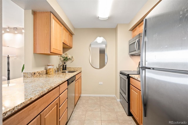 kitchen with a sink, light brown cabinets, light stone countertops, appliances with stainless steel finishes, and light tile patterned flooring