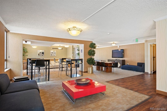 living area with baseboards, ornamental molding, a textured ceiling, and wood finished floors