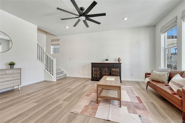 living room featuring ceiling fan, light hardwood / wood-style flooring, and a textured ceiling