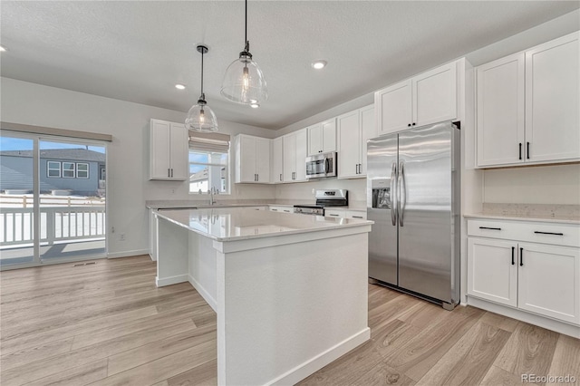 kitchen with appliances with stainless steel finishes, white cabinetry, hanging light fixtures, a center island, and light wood-type flooring