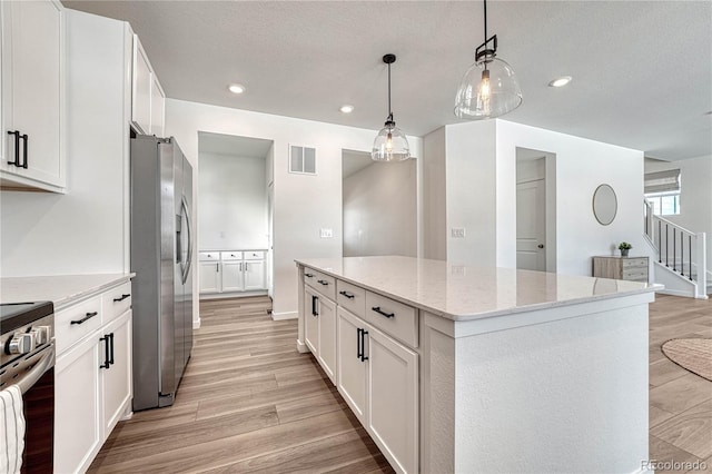 kitchen featuring light stone counters, decorative light fixtures, appliances with stainless steel finishes, a kitchen island, and white cabinets