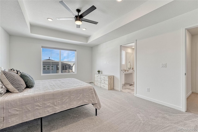 bedroom featuring light carpet, connected bathroom, a tray ceiling, and ceiling fan