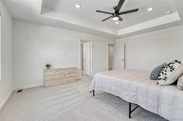 bedroom featuring a tray ceiling, light colored carpet, and ceiling fan