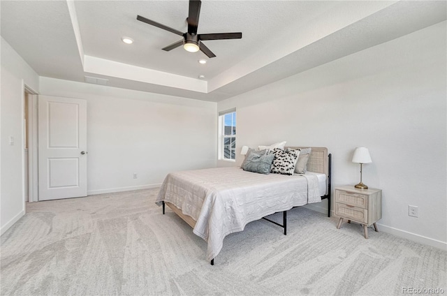 carpeted bedroom with ceiling fan and a tray ceiling